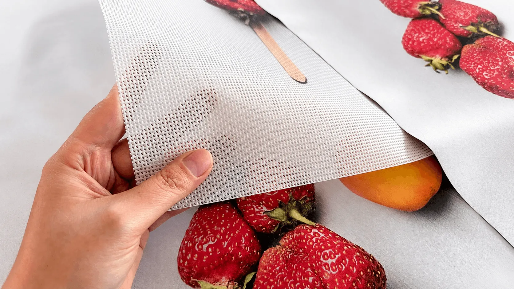 Hand hält offenporiges Mesh über unterschiedlich bedruckten Bannermaterialien