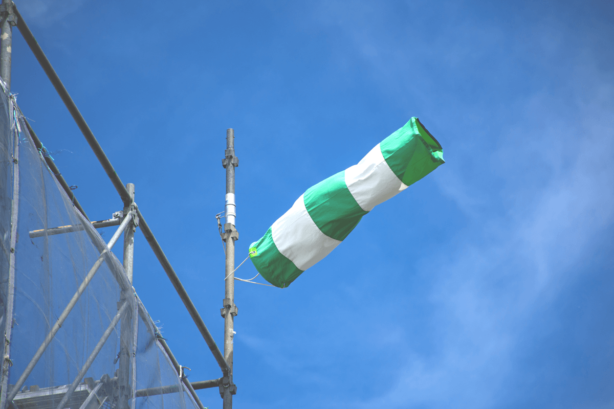 Grün-weiße Windhose an einem Gerüst zeigt deutlich einwirkenden Wind.