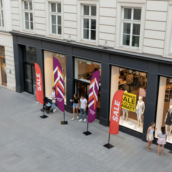 Mehrere Beachflags mit Aufdruck „SALE“ und „Fashion Flow“ vor einem Modegeschäft in der Innenstadt – auffällige Werbefahnen zur Bewerbung saisonaler Rabattaktionen.