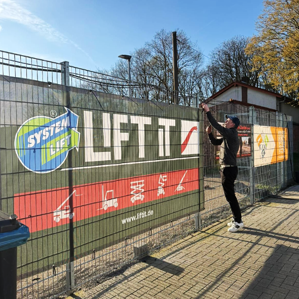 Montage eines Bauzaunbanners mit Lift-it Sponsorenlogo am Stadionzaun – einfache Befestigung